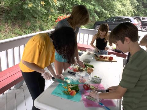 a group of teens cutting fruits and vegetables on a table