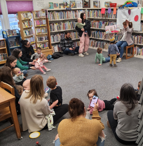 A group of children and parents sitting in circle while a librarian reads