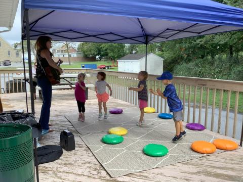 a woman playing a guitar while a group of children dance along