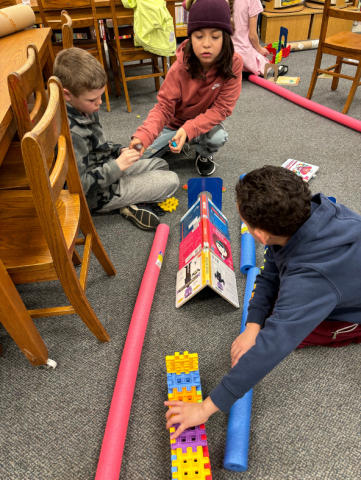 A group of children sit on the floor while a librarian guides them in an activity.